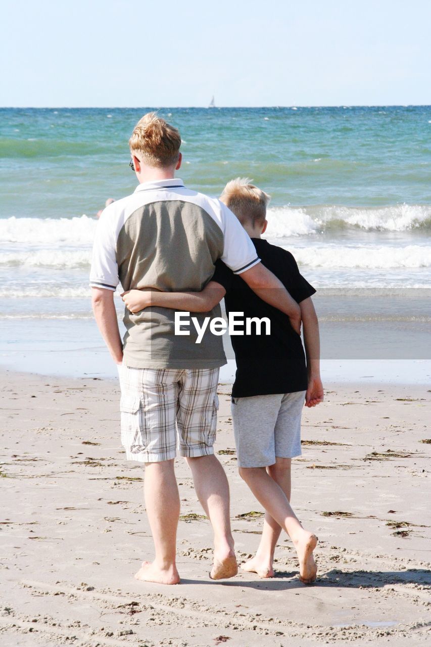 Rear view of father and son walking at beach