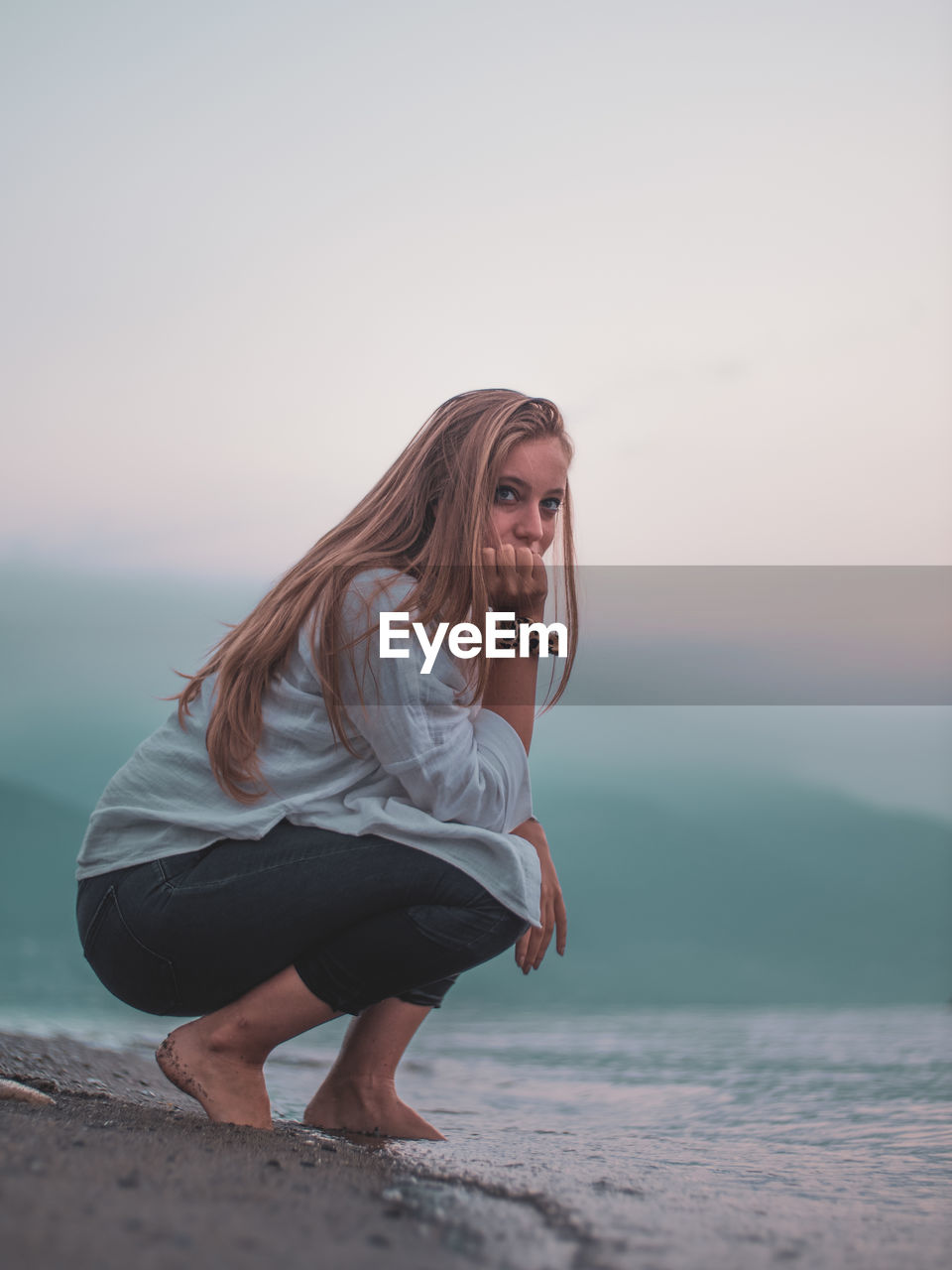 Portrait of beautiful young woman on beach against sky during sunset