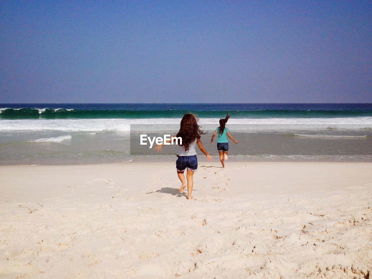 Rear view of sisters on beach against sky