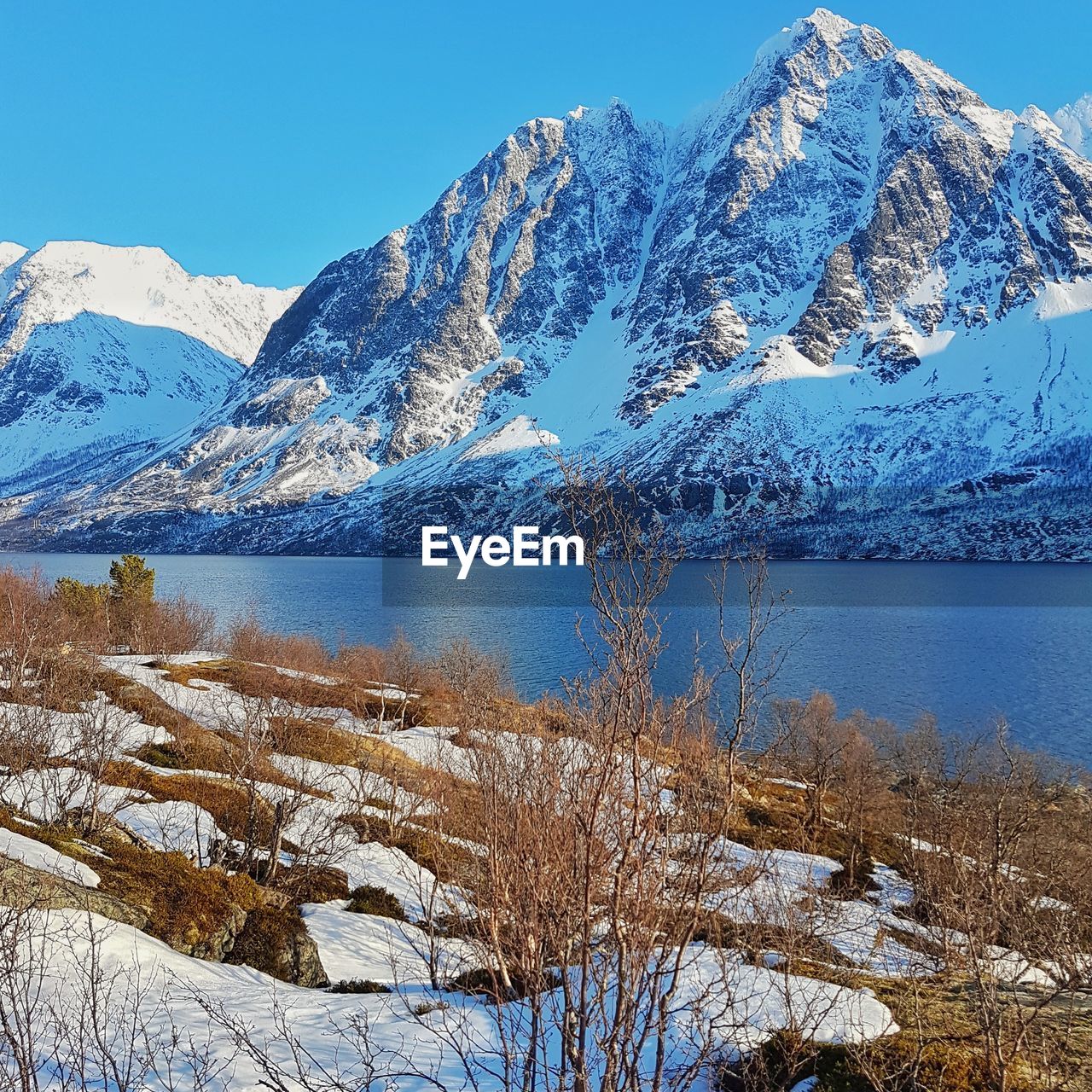 Frozen lake by snowcapped mountains against sky