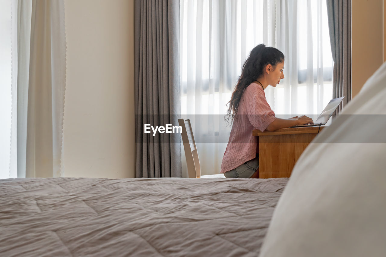 Beautiful brunette using notebook in at home in her bedroom. photo with selective focus