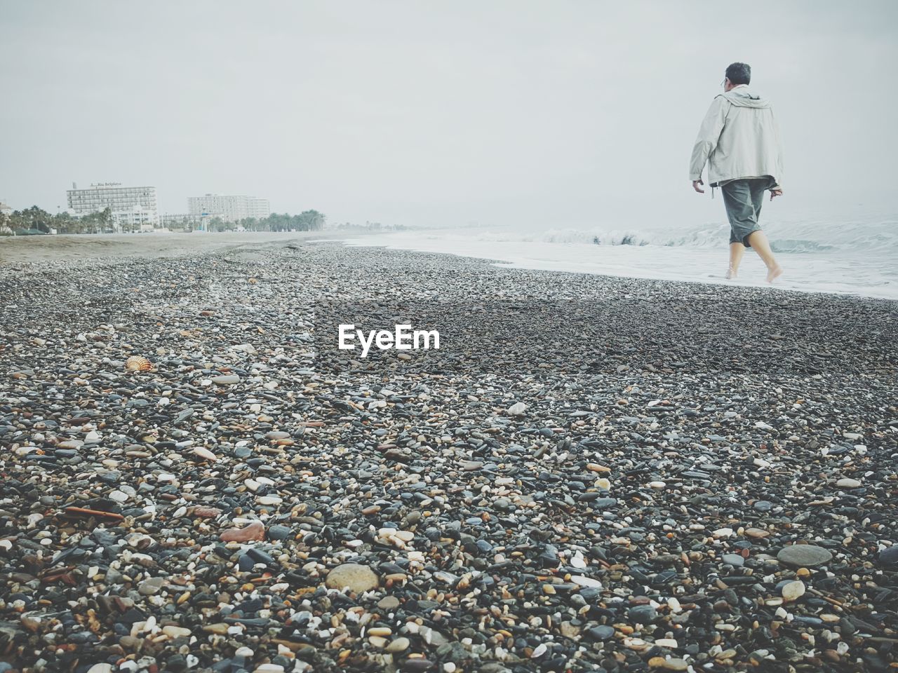 Rear view of man walking at beach against clear sky