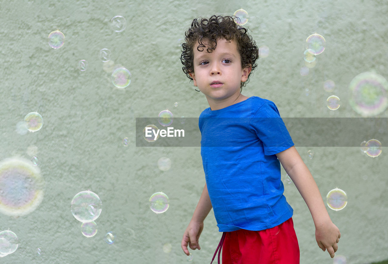 4-5 year old boy with curly hair in his backyard, playing with soap bubbles
