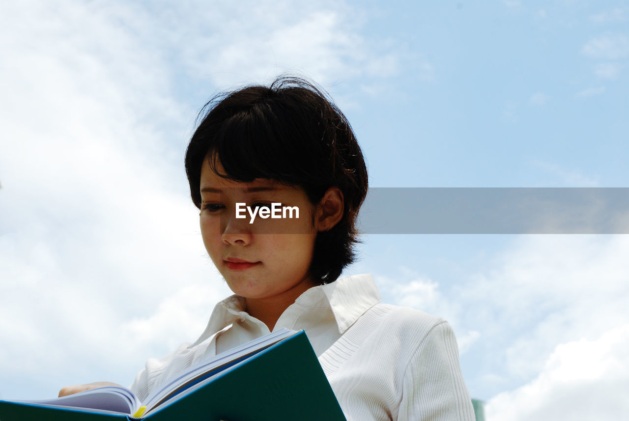 Low angle view of woman reading diary against sky