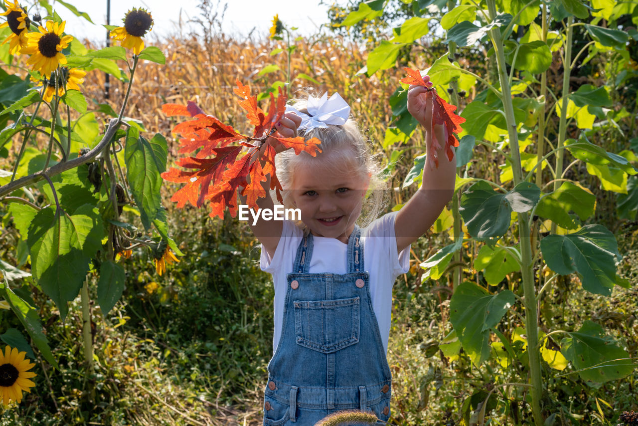 PORTRAIT OF SMILING GIRL STANDING BY PLANTS
