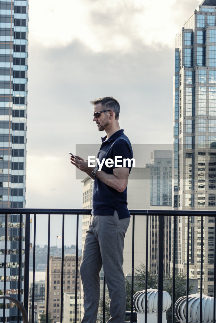 Side view of businessman using smart phone while standing on building terrace