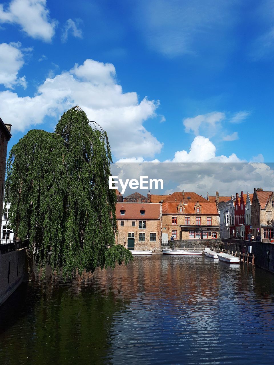 Buildings and boats by canal against sky in bruges