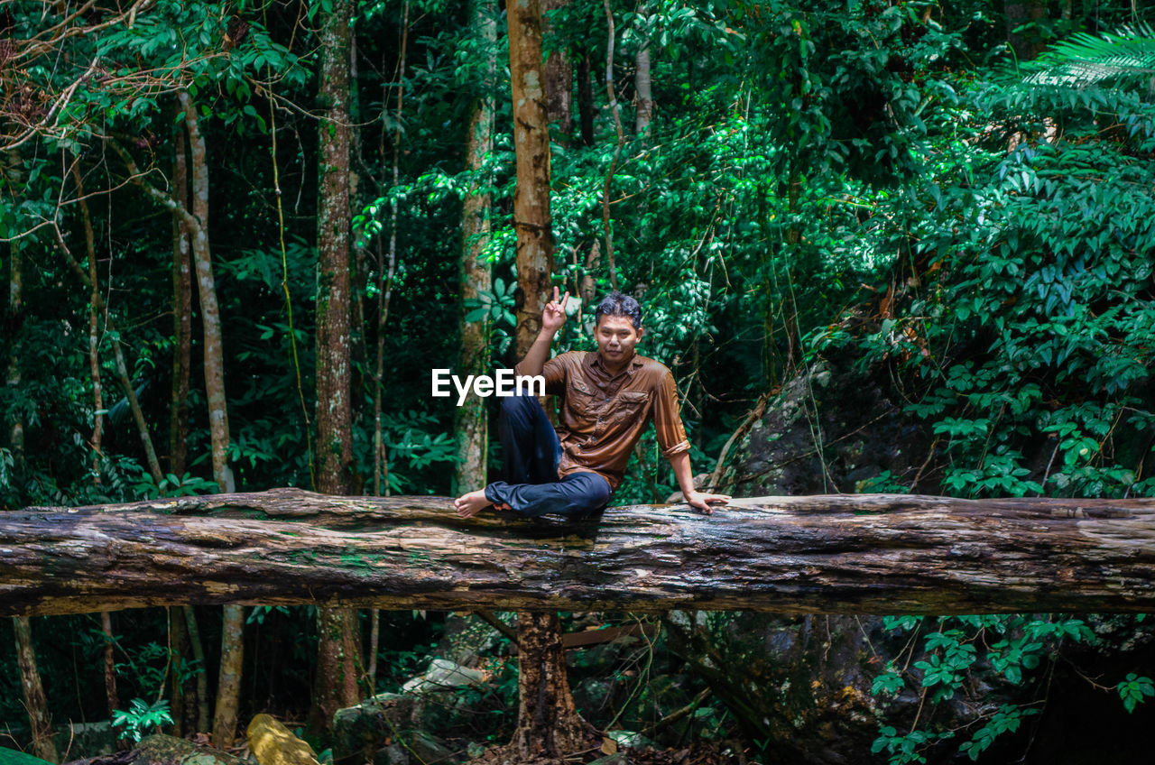 Portrait of man sitting on tree trunk in forest