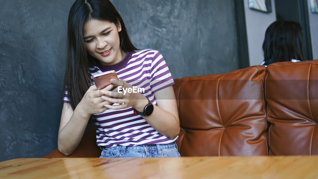 Smiling young woman using smart phone sitting at table in cafe