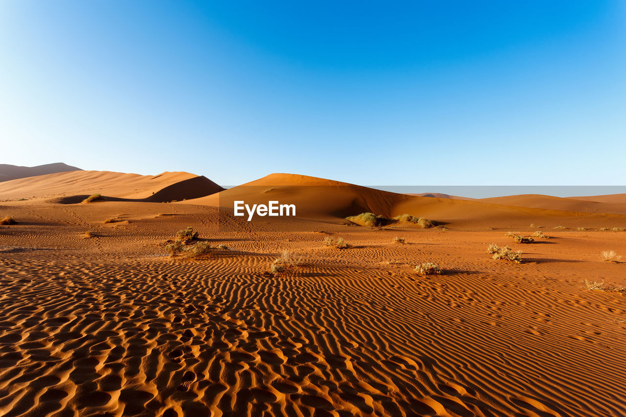 Sand dunes in desert against clear blue sky