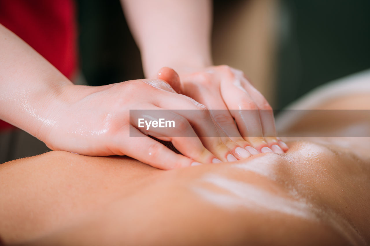 Massaging with massage oil, hands of a female massage therapist massaging a female client