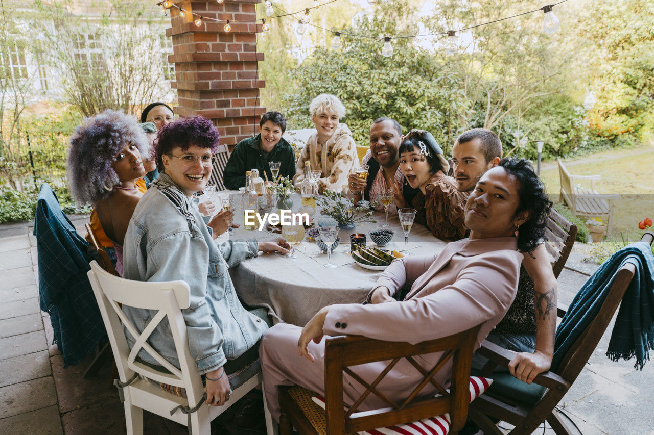 Portrait of happy friends from lgbtq community sitting at dining table during dinner party in back yard