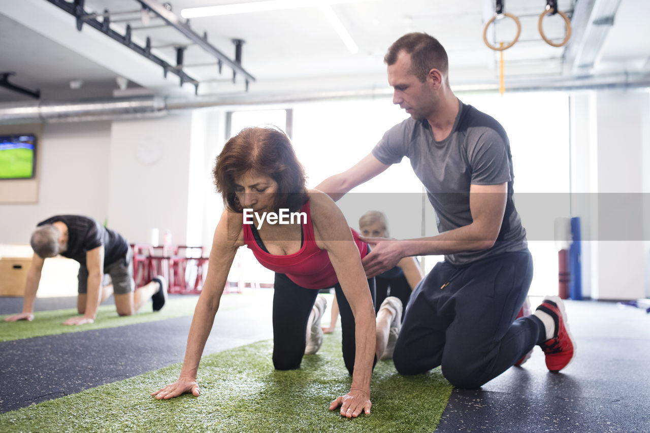 Personal trainer assisting senior woman in gym