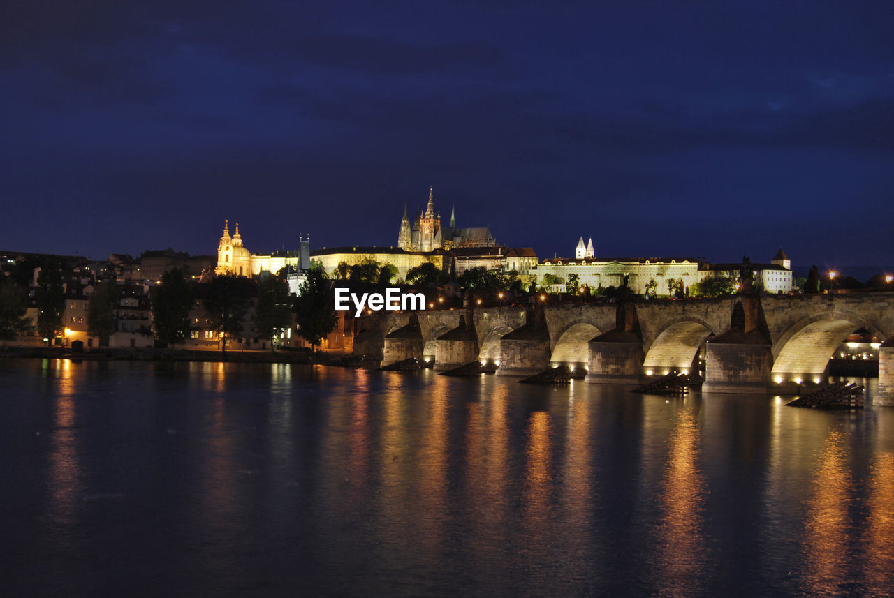 ILLUMINATED BUILDINGS BY RIVER AGAINST SKY