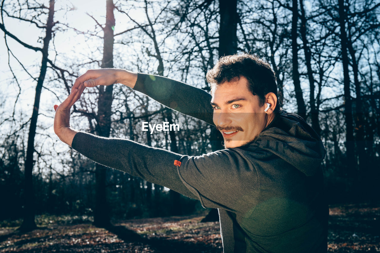 Runner is doing stretching in the woods. man with blue eyes and mustache is training in the park.