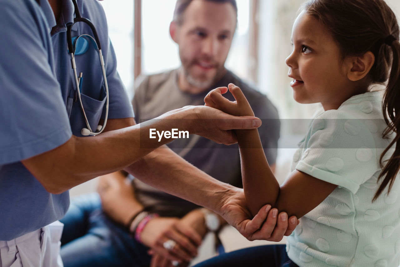 Midsection of nurse examining girl sitting with father at clinic