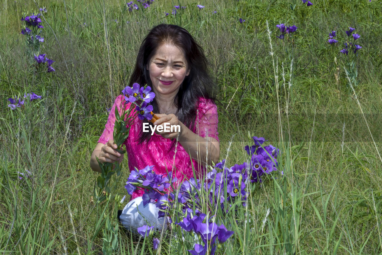 PORTRAIT OF A SMILING YOUNG WOMAN WITH PURPLE FLOWER