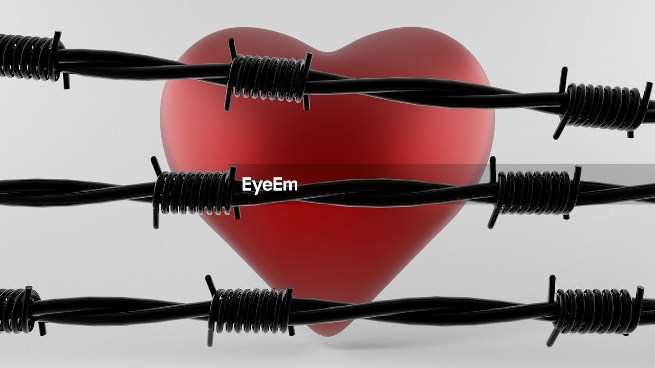 Close-up of heart shape and barbed wires against white background