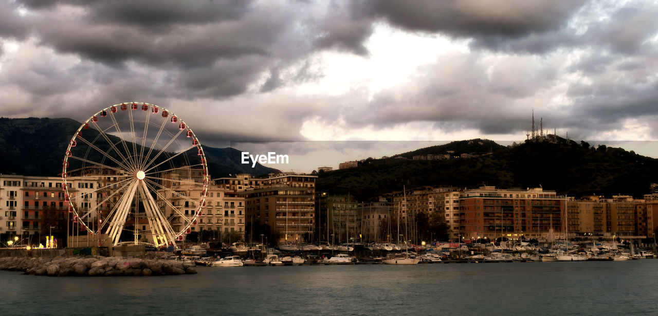 Ferris wheel in city against cloudy sky