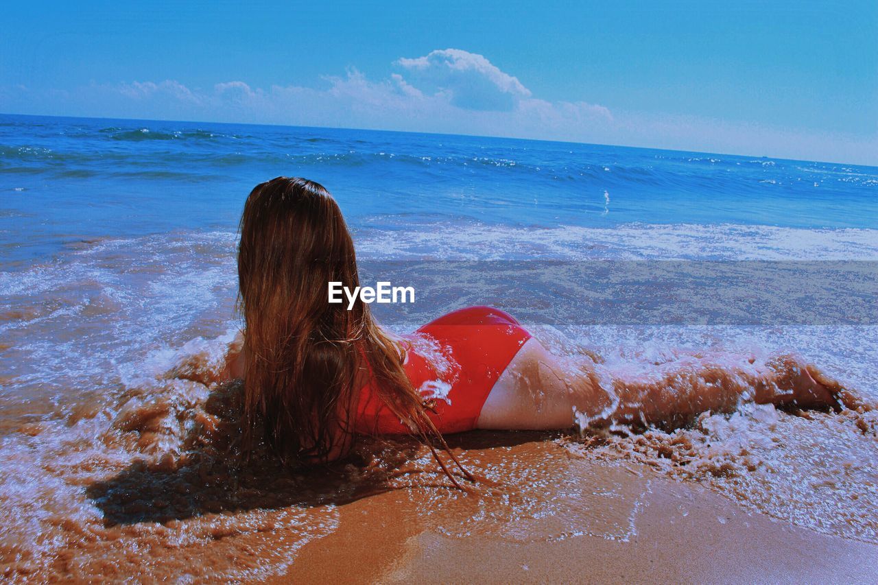 Full length of woman in swimwear lying at beach against sky during sunny day