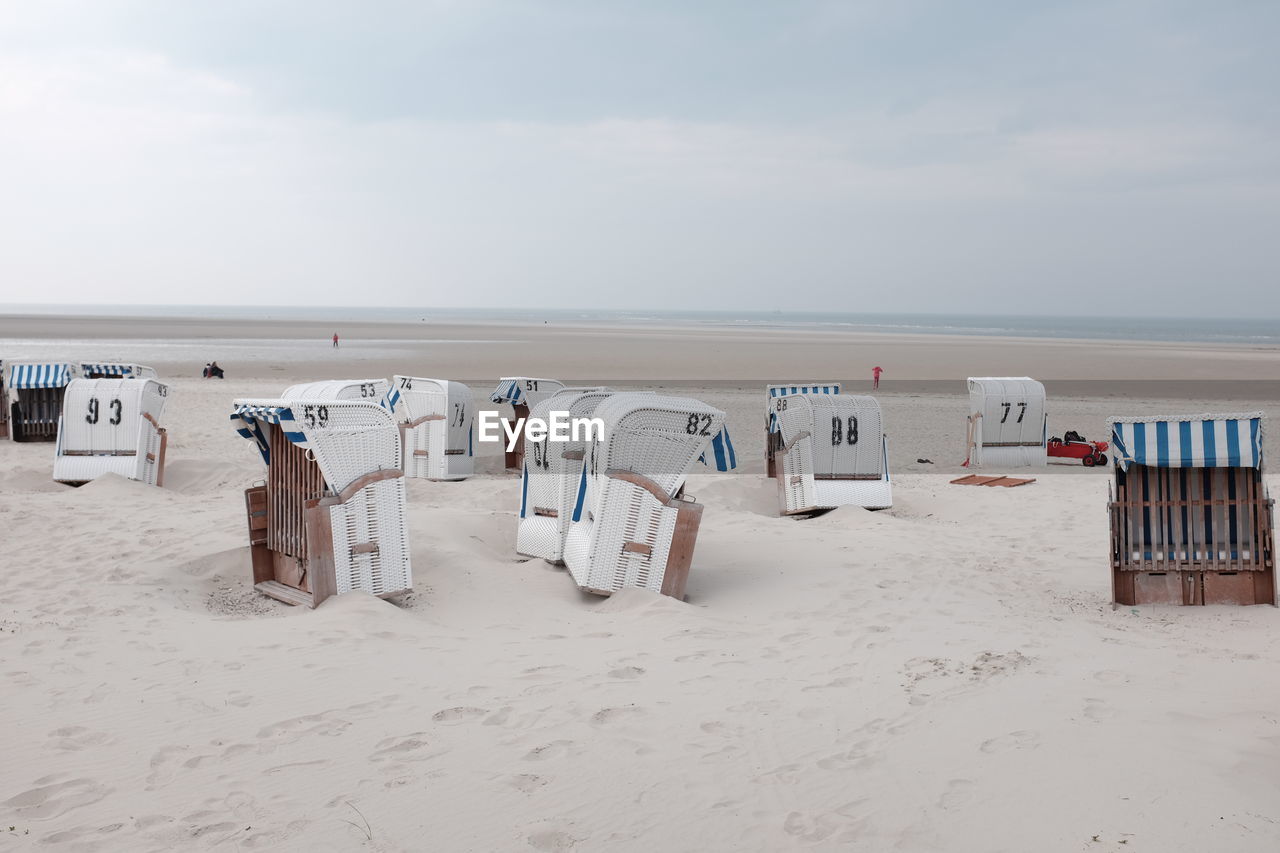 Hooded beach chairs on sea shore against sky