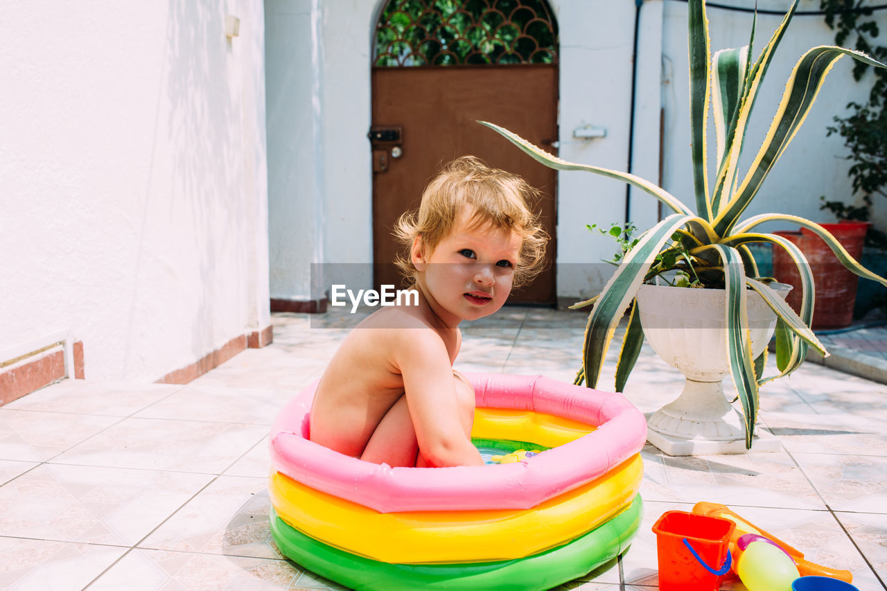 Cute child has fun in inflatable pool with toys in summer in backyard.