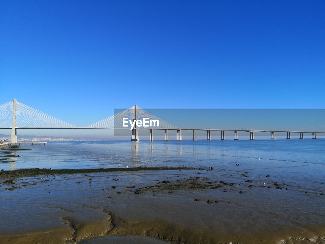 Suspension bridge over sea against clear blue sky