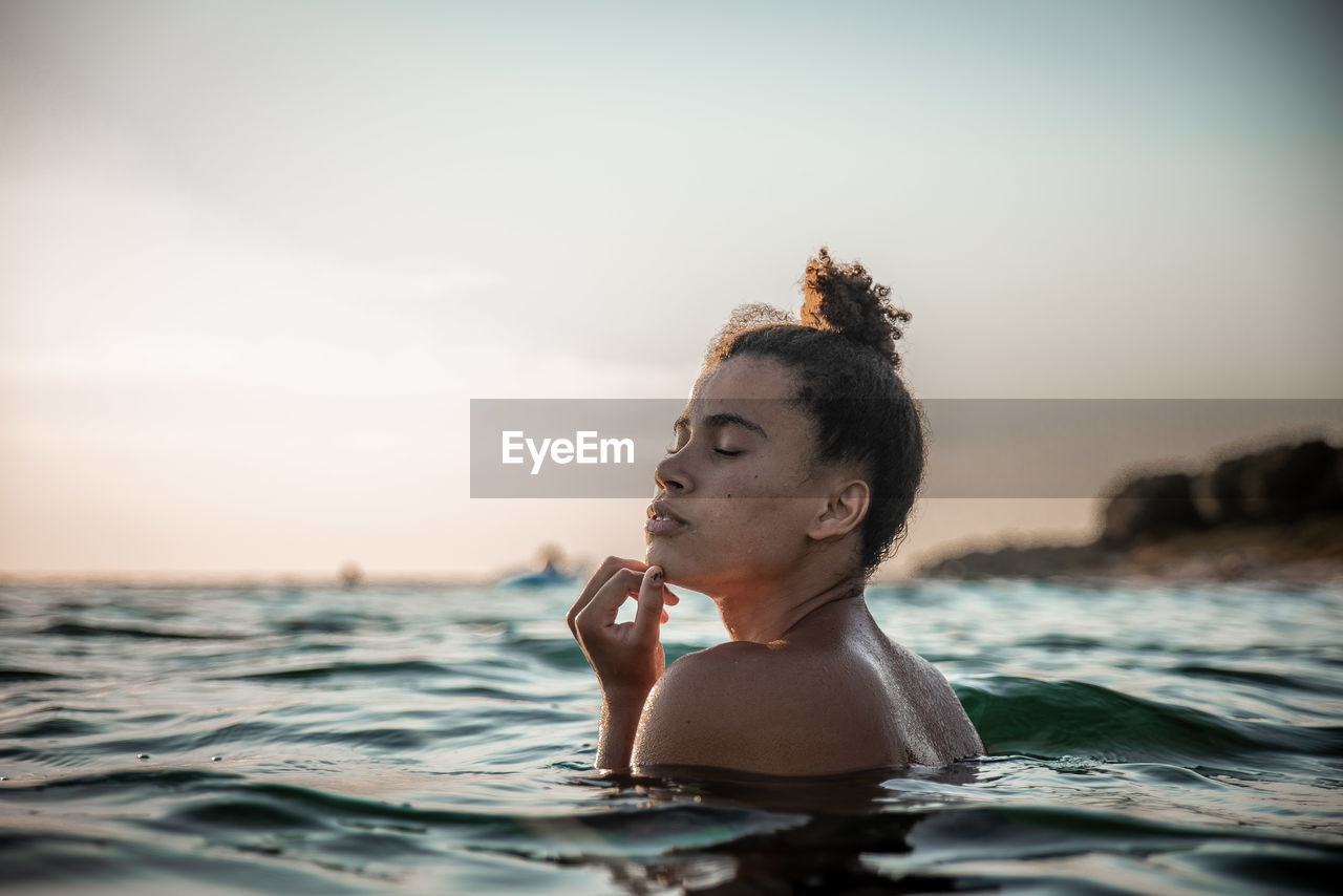 Shirtless young woman swimming in sea against sky