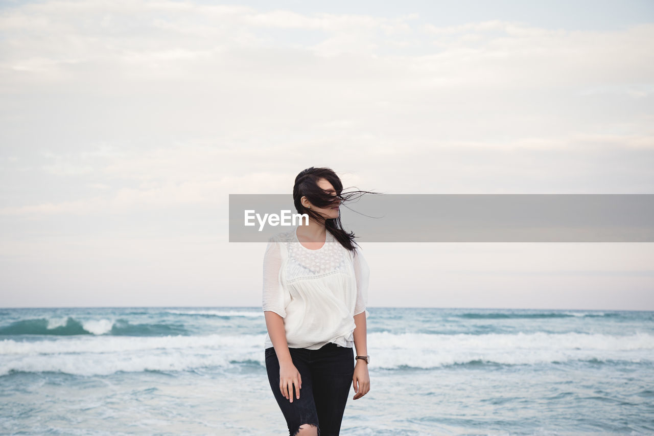 Portrait of a young beautiful woman with windy hair standing by the sea