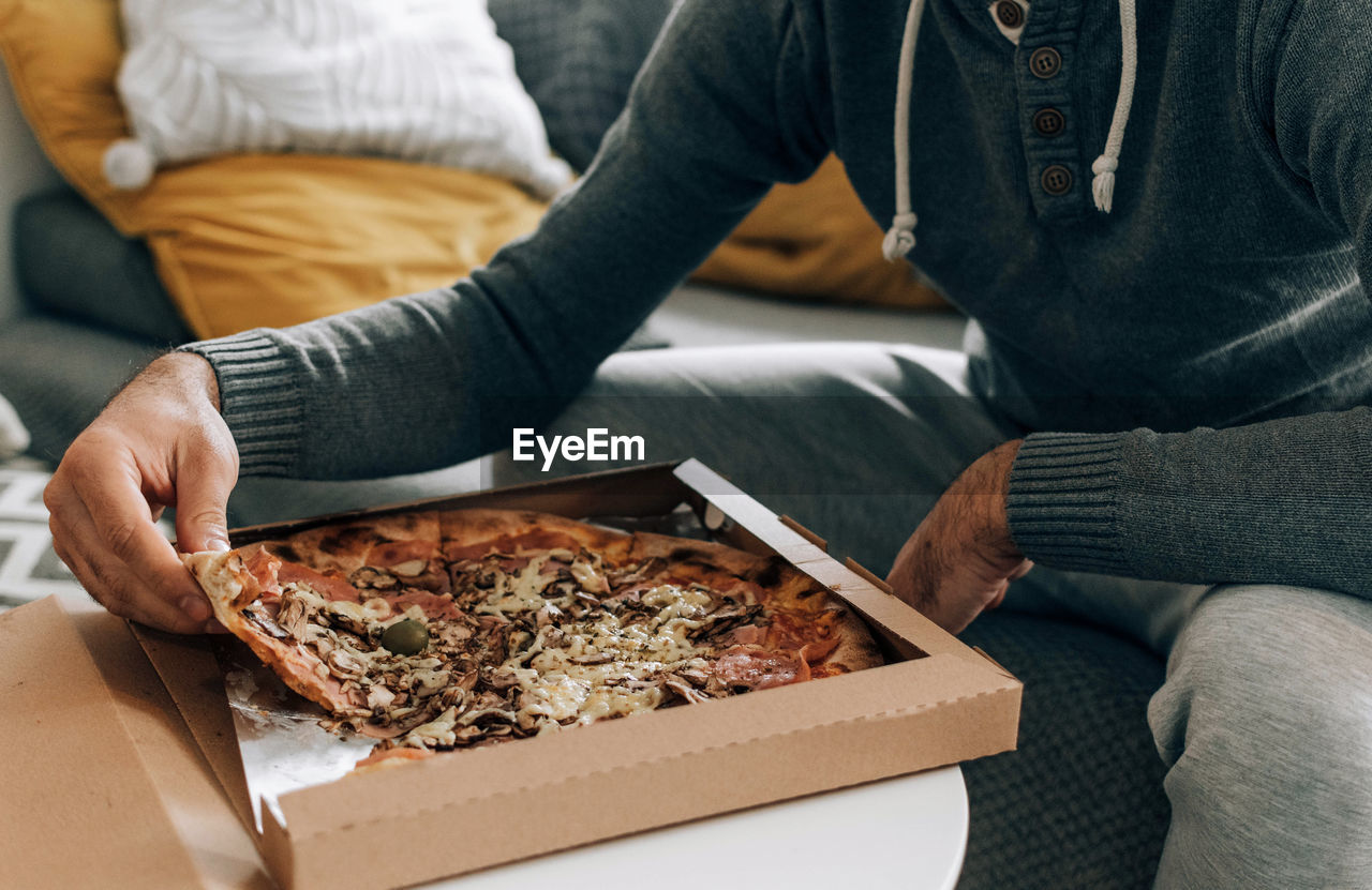 Man sitting on couch, eating pizza. pizza box, pizza delivery.