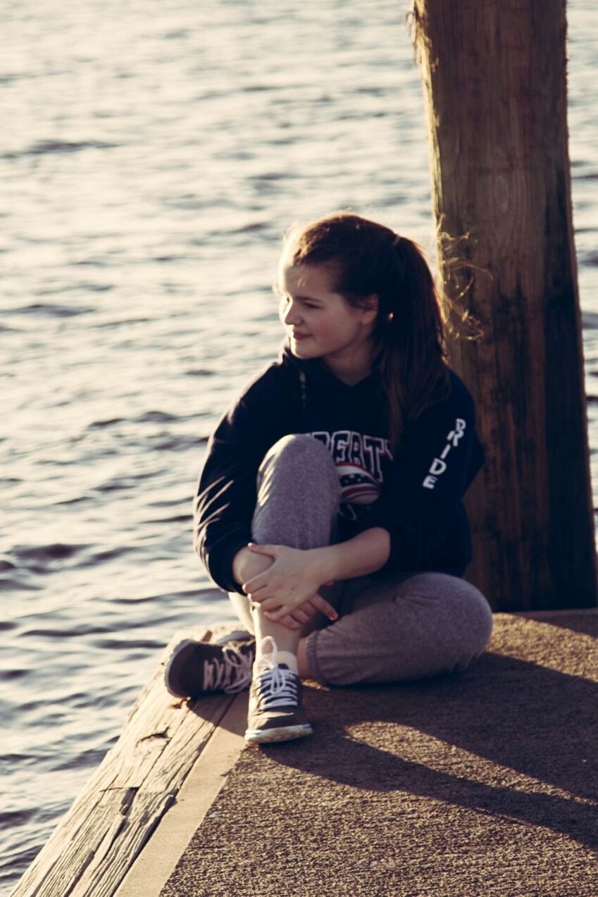 Full length of teenage girl sitting by lake