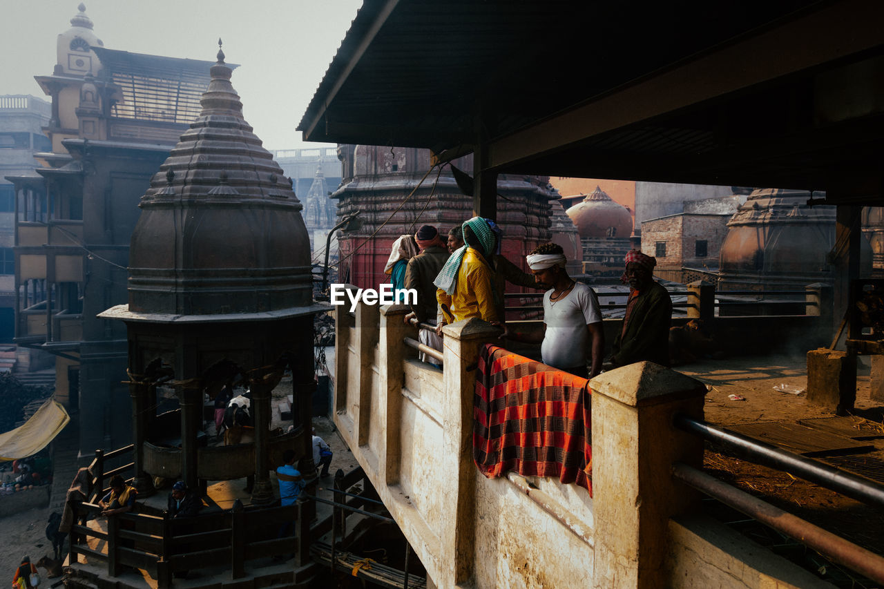 Varanasi, india - february, 2018: locals standing on balcony of city construction in old holy town with ancient buildings and temples