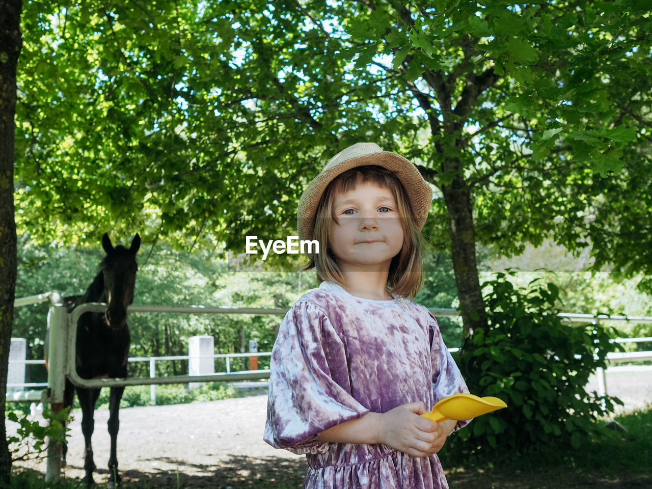 Portrait of small girl wearing lilac dress and summer hat and horse