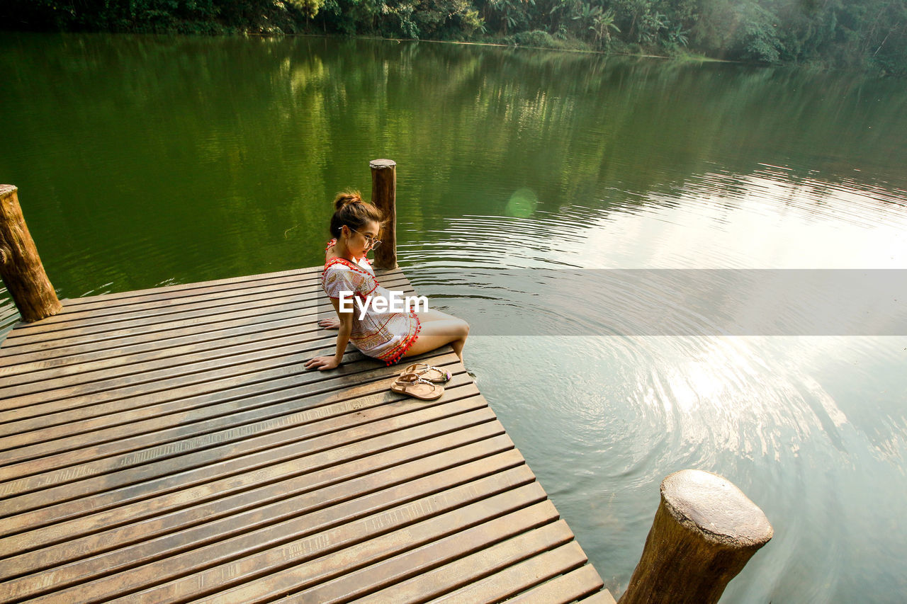 Woman sitting on pier over lake