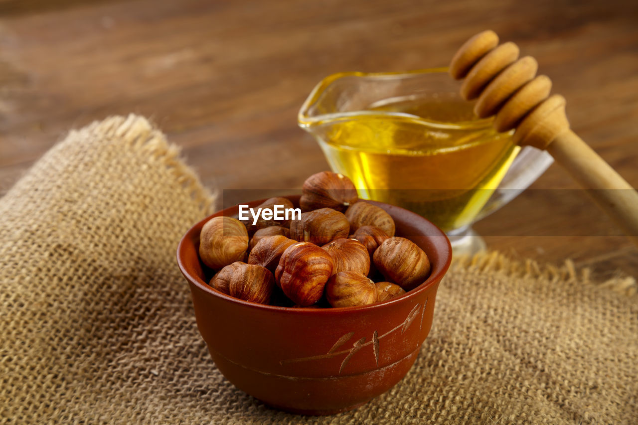 Hazelnuts in a bowl on a sacking next to honey with a spoon on a wooden table. horizontal photo