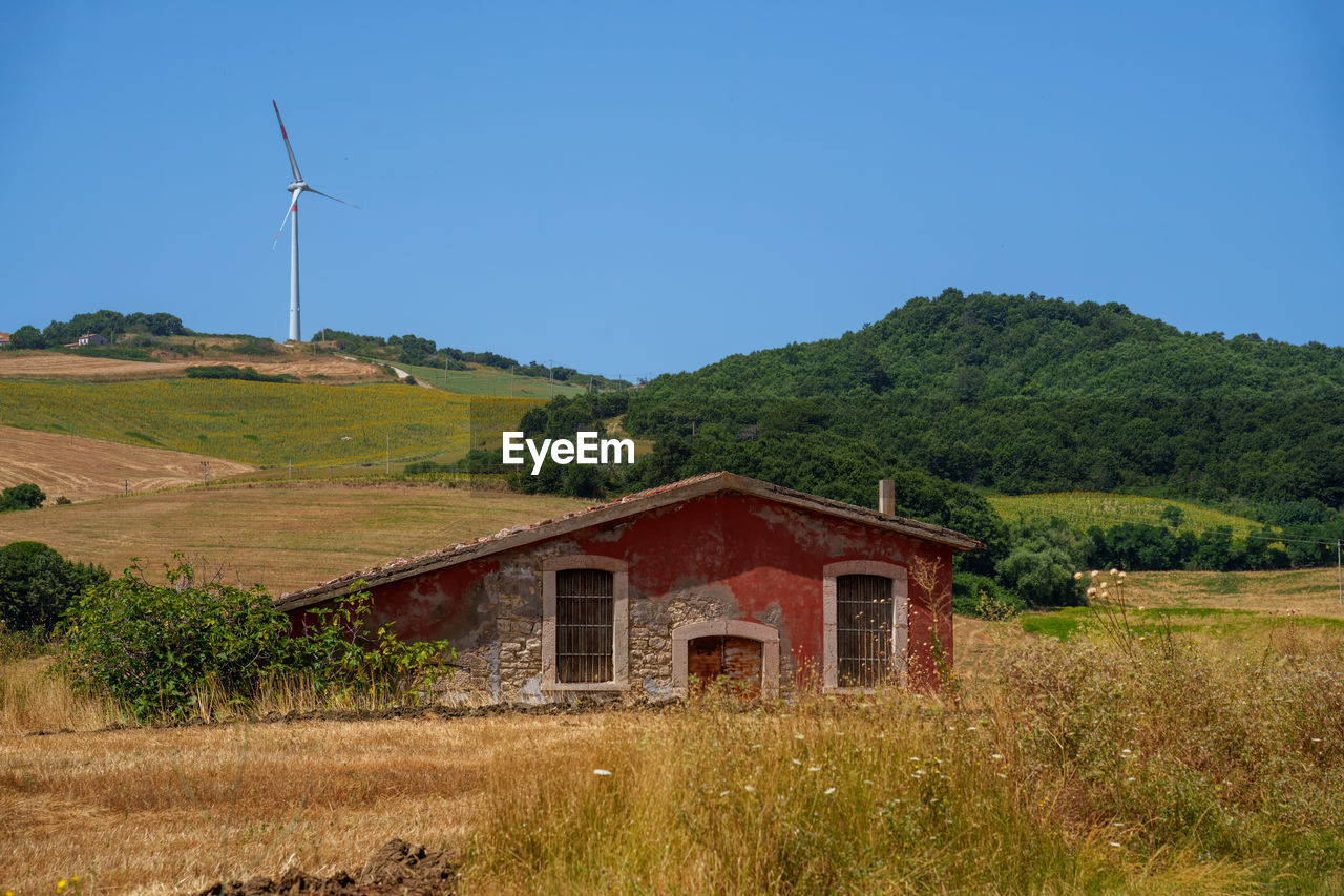 windmill, environment, landscape, rural area, environmental conservation, turbine, architecture, wind turbine, rural scene, built structure, renewable energy, wind power, sky, alternative energy, building, nature, land, plant, building exterior, power generation, village, hill, grass, field, house, agriculture, scenics - nature, beauty in nature, farm, no people, non-urban scene, blue, clear sky, residential district, prairie, mill, social issues, outdoors, tree, day, technology, tranquility, grassland, plain, agricultural building, green, travel destinations, travel, tranquil scene, history