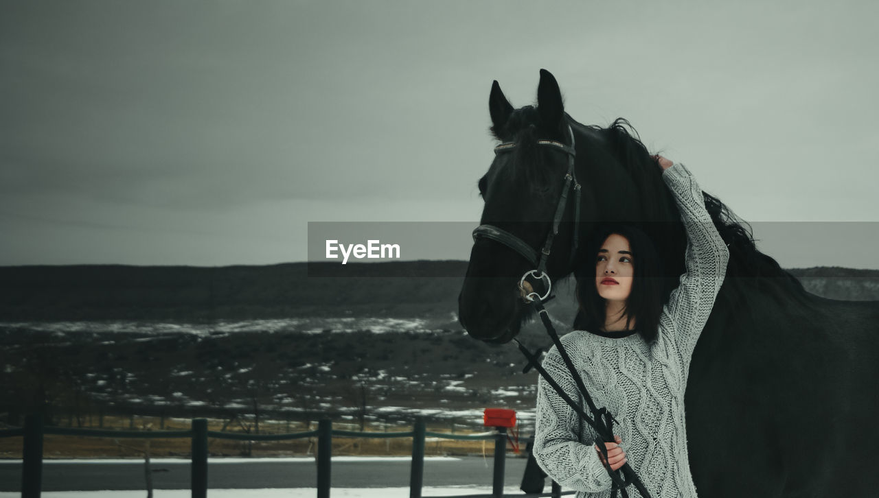 Woman standing by horse against sky during winter