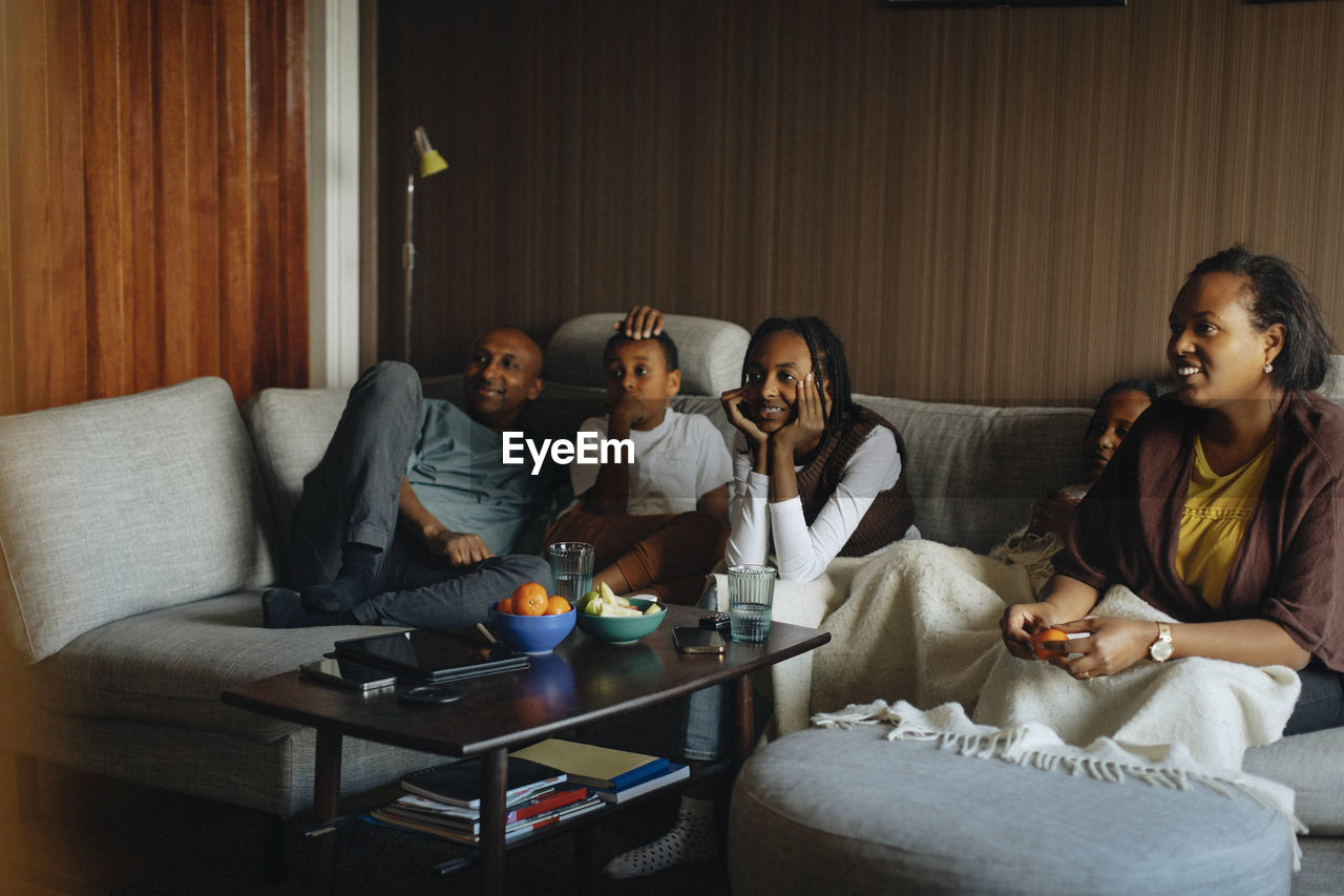 Family watching tv together while sitting on sofa at home