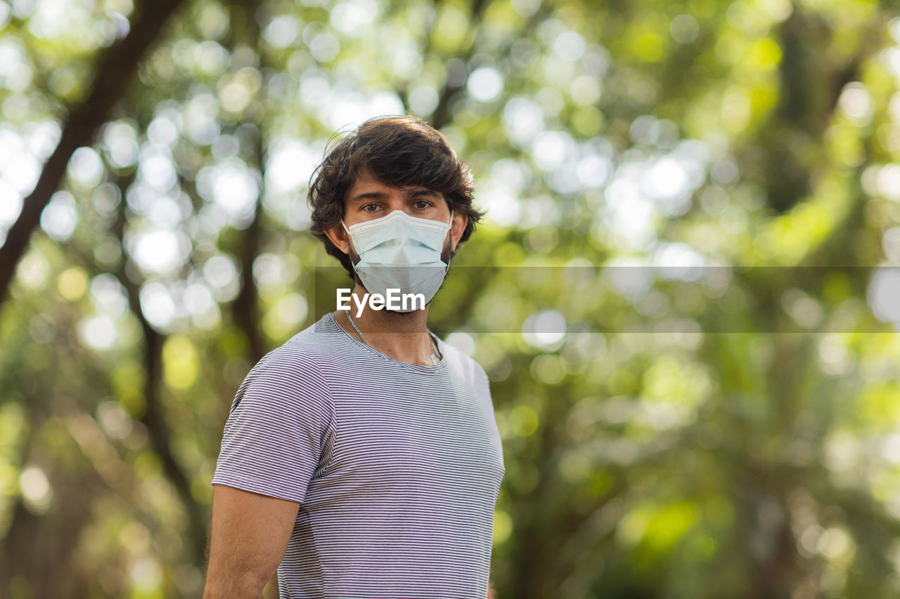 Handsome man wearing a medical protective mask on his face on a sunny day at park.