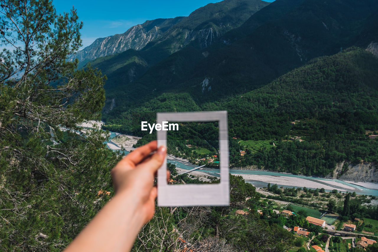 Cropped hand of woman holding picture frame against landscape