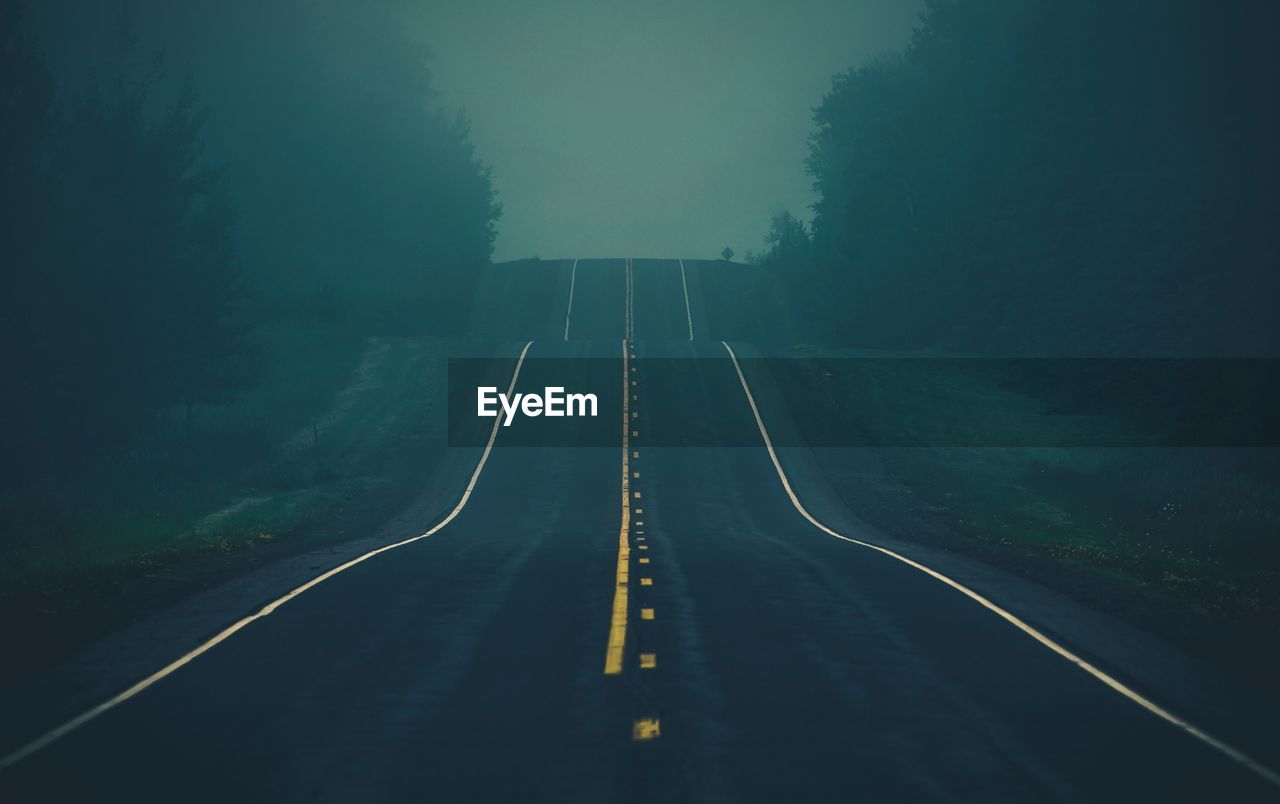 Empty road along trees during foggy weather