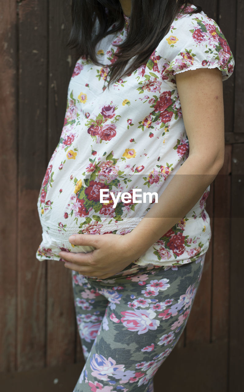 Midsection of pregnant woman standing against wooden door