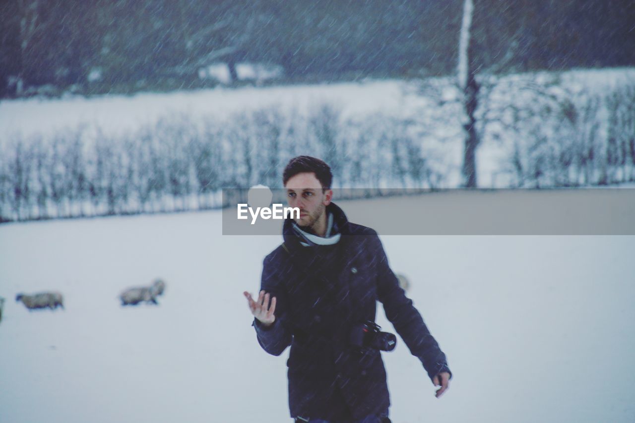 Man catching snow ball while standing on field