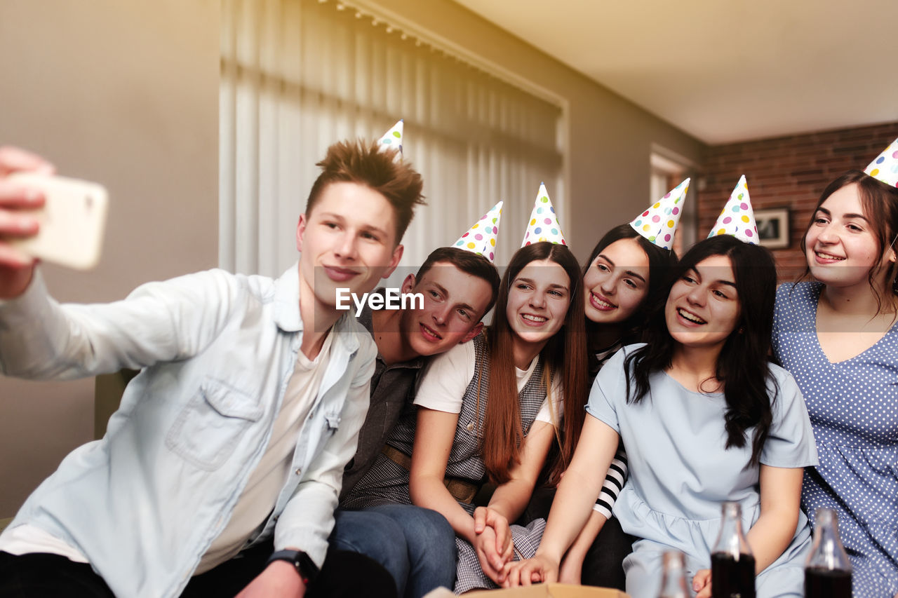 Group of best friends with festive cap taking selfie at birthday party