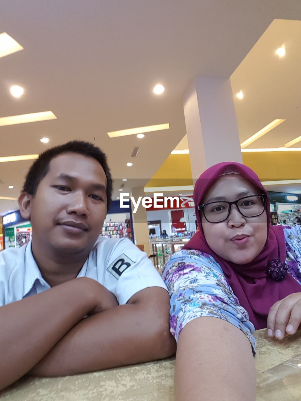 PORTRAIT OF SMILING YOUNG COUPLE SITTING IN OFFICE