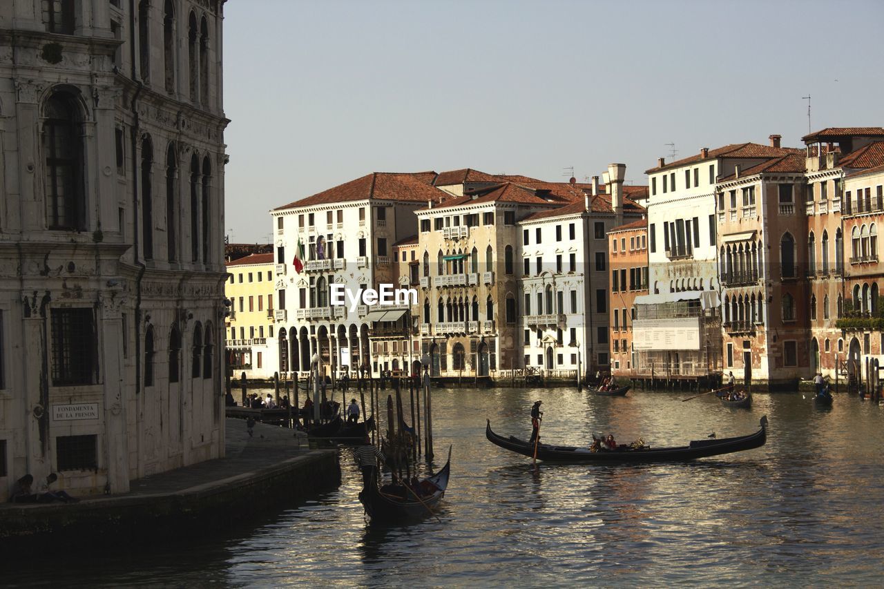 Gondolas moving on canal amidst buildings against clear sky