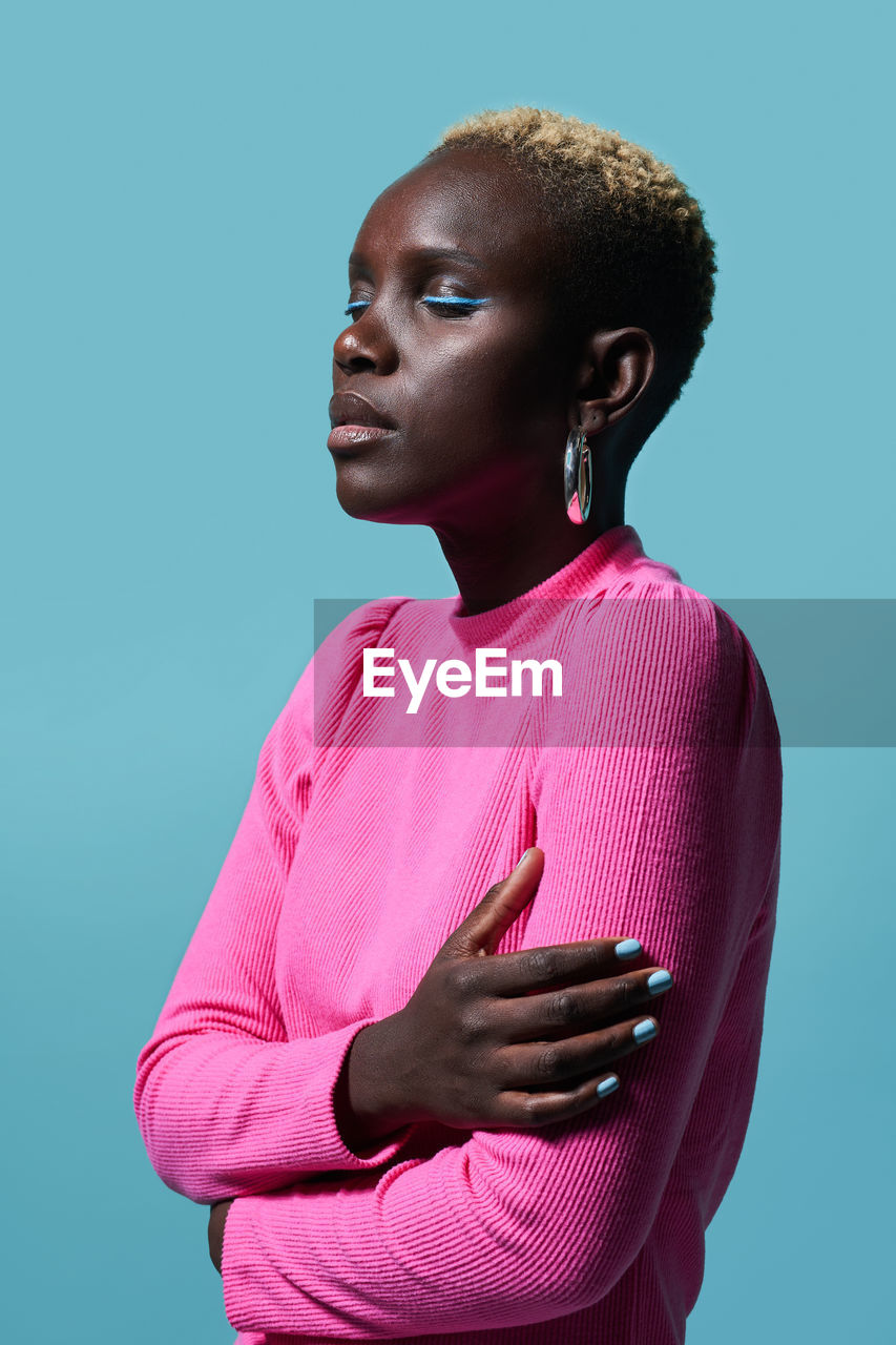 Side view of an african woman wearing a pink sweater styled with her arms crossed