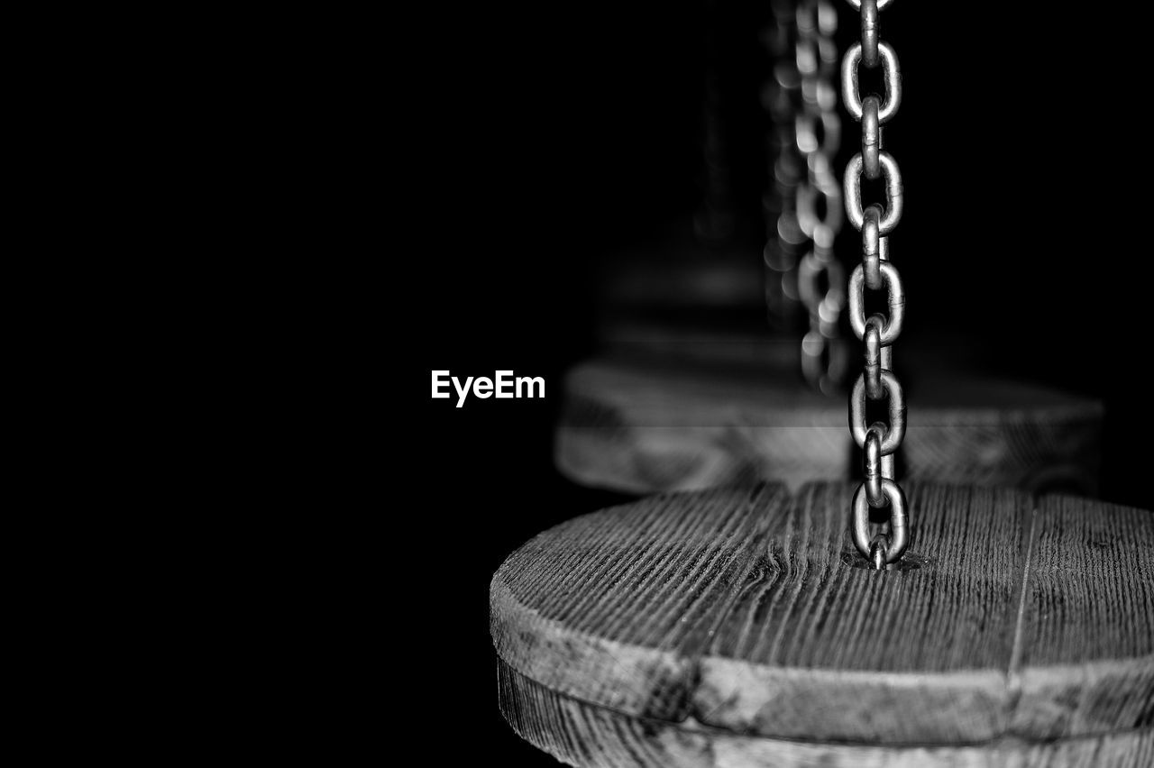 Close-up of wood hanging to chains against black background