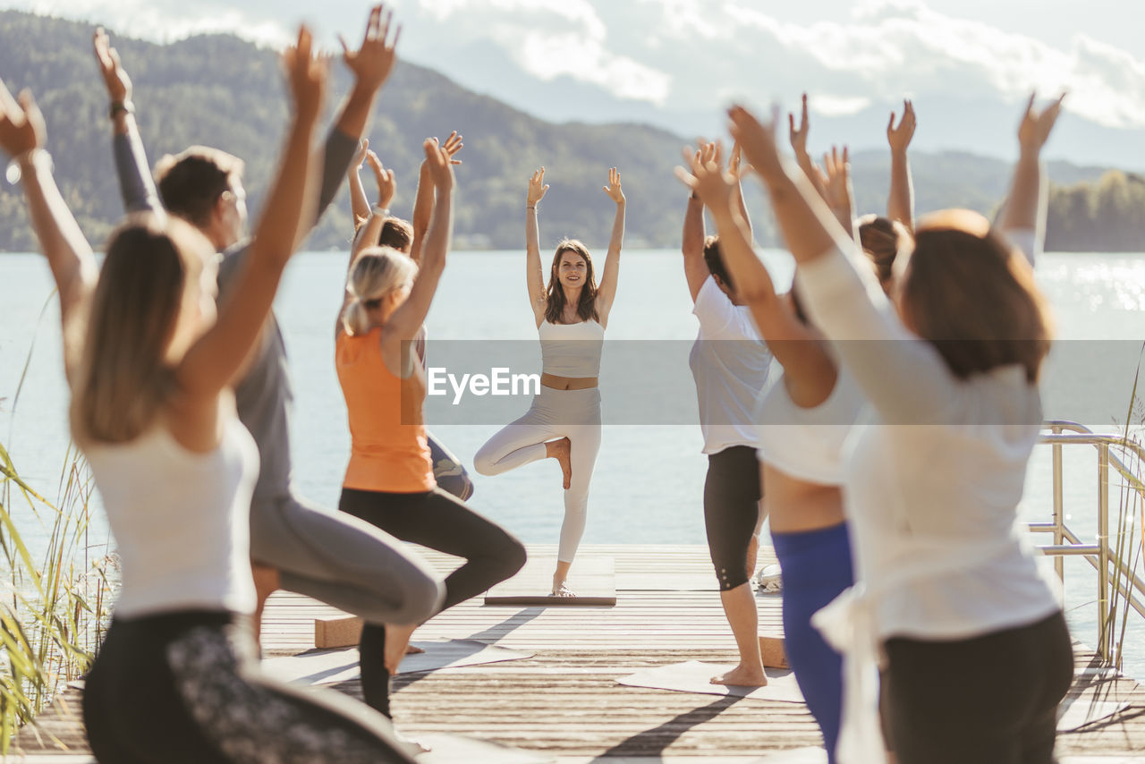 Female instructor teaching vrikshasana to men and women during yoga class