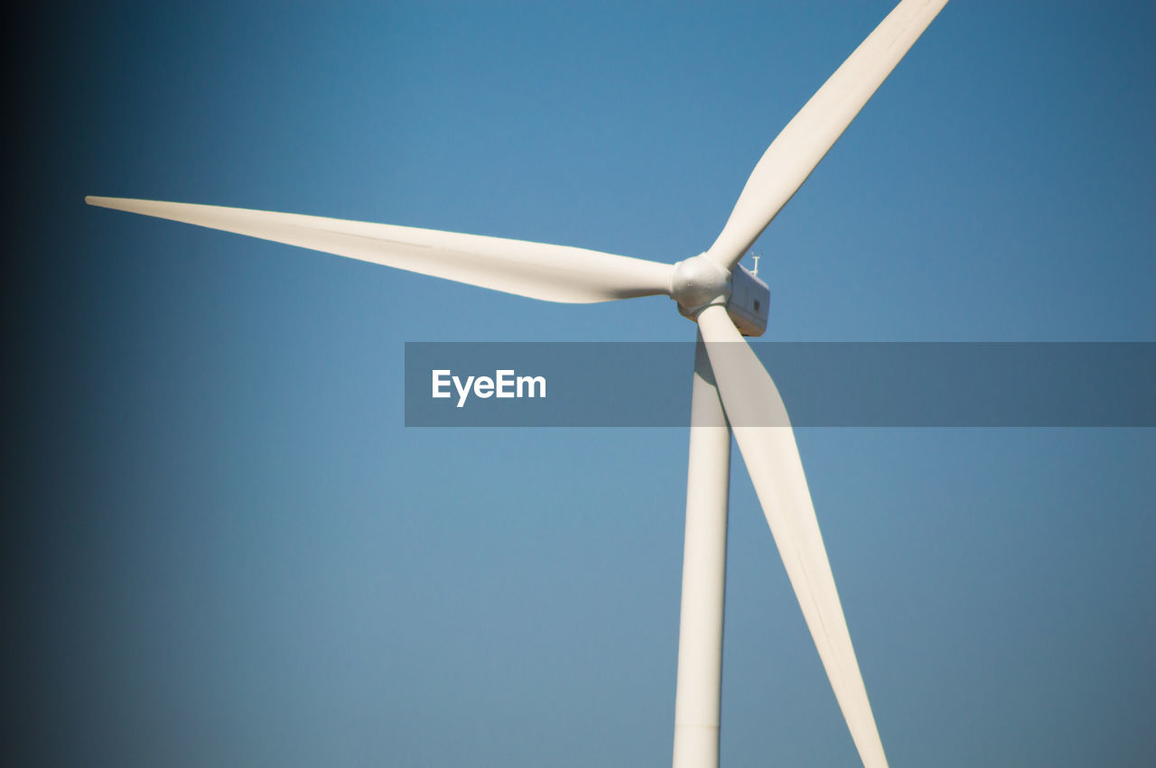 LOW ANGLE VIEW OF WIND TURBINES AGAINST BLUE SKY